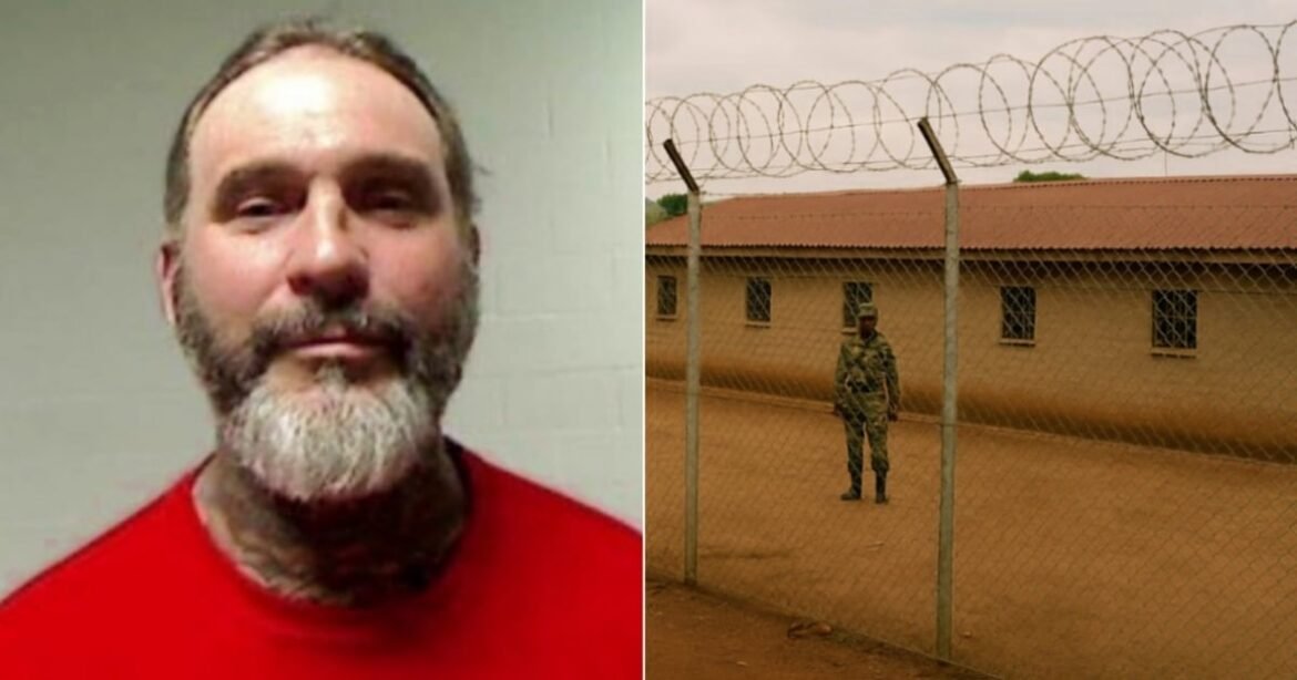 Un soldado hace guardia afuera de una prisión con una cerca de alambre de púas y una fila de edificios institucionales al fondo