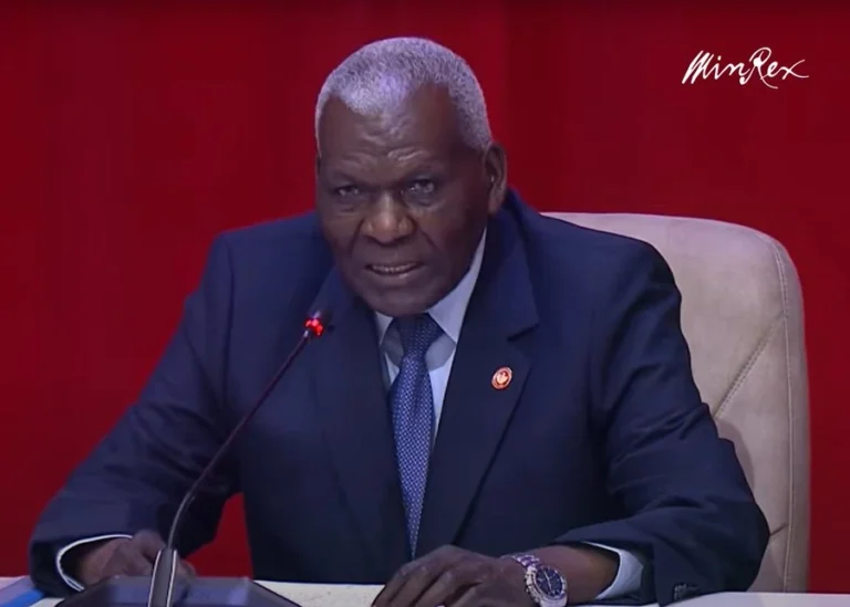 Estados Unidos Endurece Sanciones Contra la Cúpula del Régimen Cubano Man in a dark suit and blue tie sitting at a desk with a microphone against a red background, wearing a wristwatch.